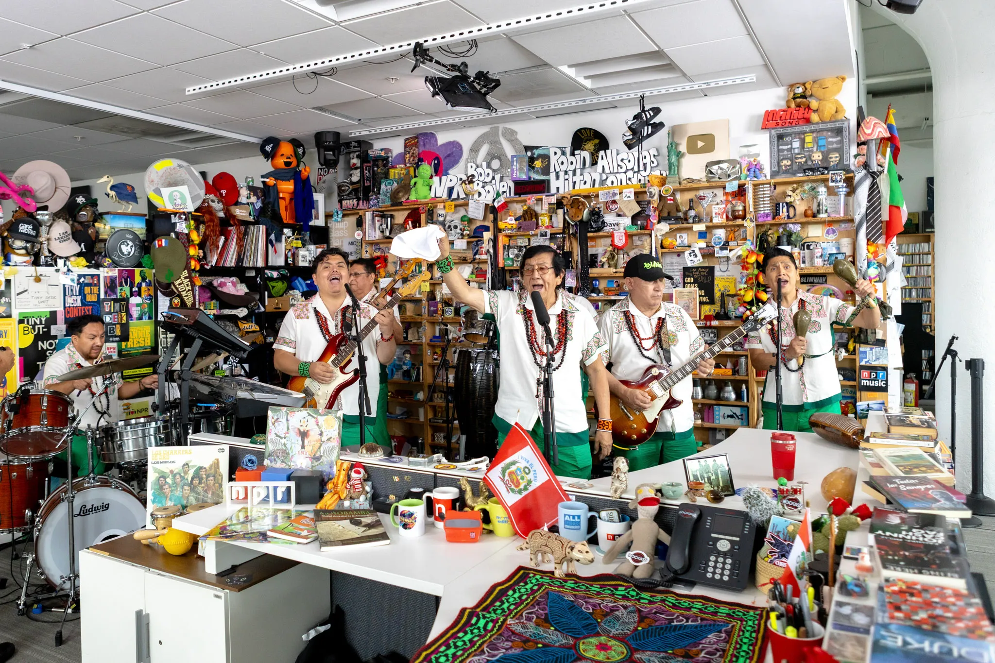 Los Mirlos performing at the NPR Tiny Desk in shirts embroidered with kené art, with a Peruvian flag on the desk